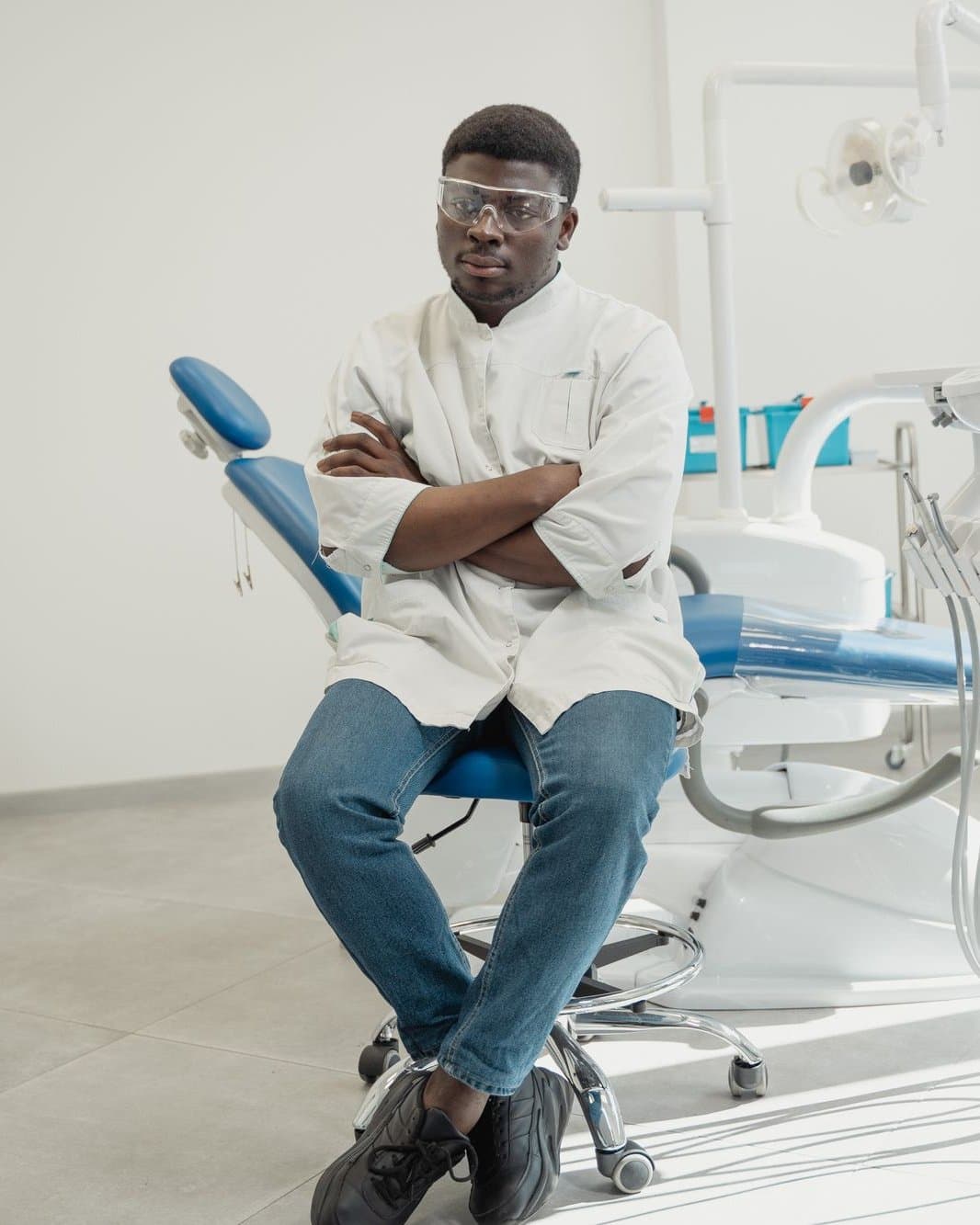 Dentista de jaleco branco sentado com os braços cruzados no consultório