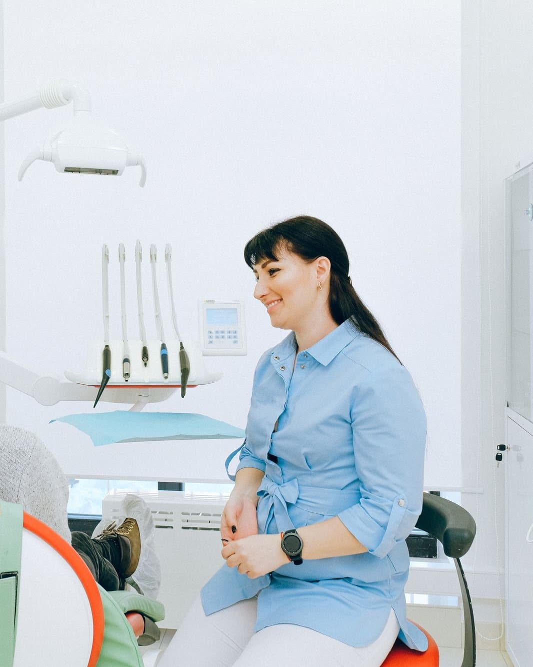 Dentista de uniforme azul sorrindo, sentada no consultório